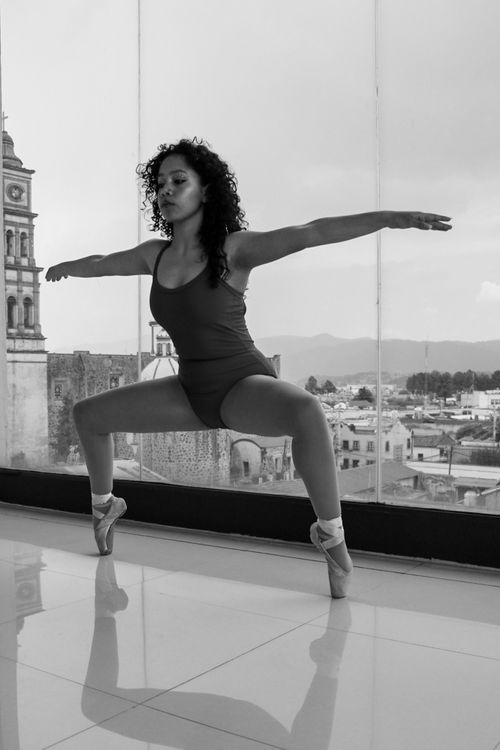 Free Ballet dancer poised in a graceful stance, silhouetted against a cityscape through large windows. Stock Photo