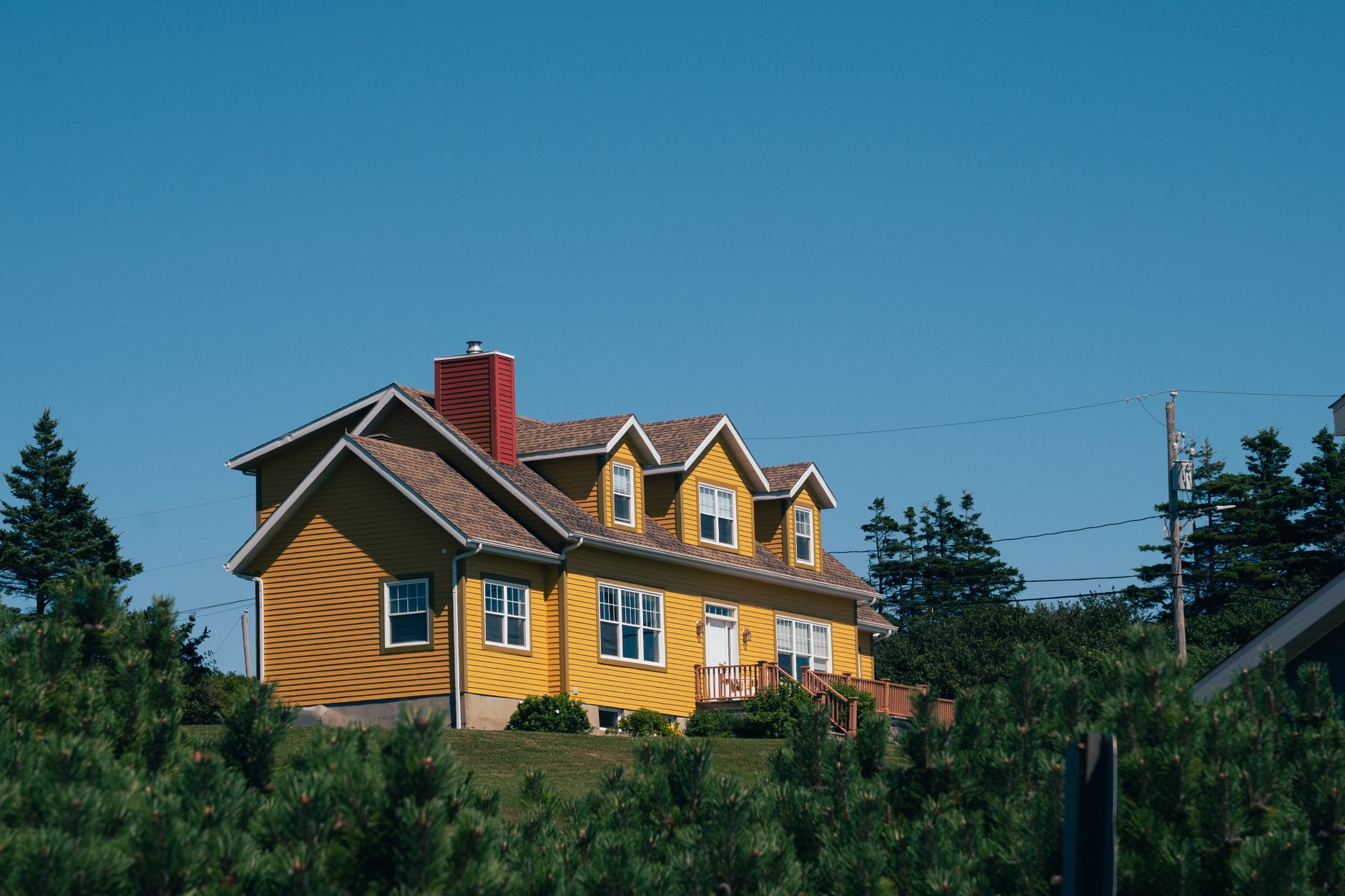 A vibrant yellow house nestled in the countryside of Percé, QC, Canada, surrounded by lush greenery.
