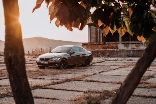Free Luxury sports car parked on pavement at sunset, framed by trees and scenic landscape. Stock Photo
