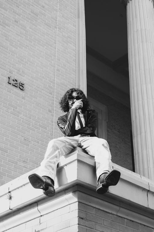 Man with Curly Long Hair Sitting on the Wall