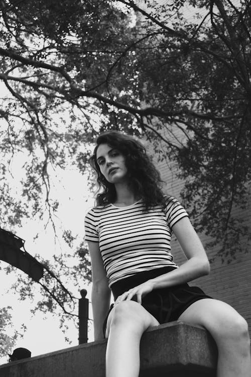 Black and White Photo of a Young Woman in Striped T-shirt Sitting on a Parapet