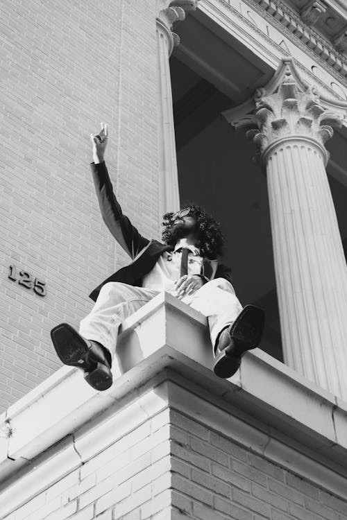 Man Sitting on the Building Wall and Raising his Hand 
