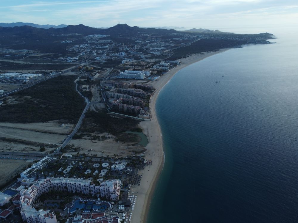 Aerial view of the Cabo San Lucas coastline showing beachfront resort hotels and sandy shore under morning light