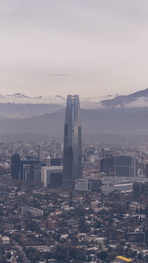 Free Aerial view of Santiago cityscape featuring the iconic Sky Costanera Tower under a foggy sky. Stock Photo