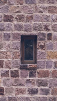 A close-up of a rustic redbrick wall featuring a solitary window, showcasing urban architectural details in Santiago, Chile.
