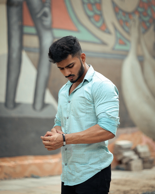 Free Portrait of a man in a blue shirt posing outdoors with urban mural backdrop. Stock Photo