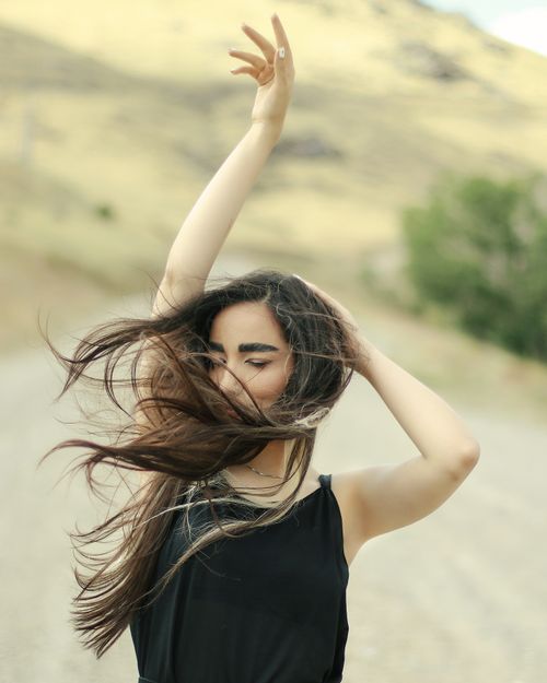 Free Portrait of a woman with long hair dancing in an outdoor setting, eyes closed and arms raised. Stock Photo