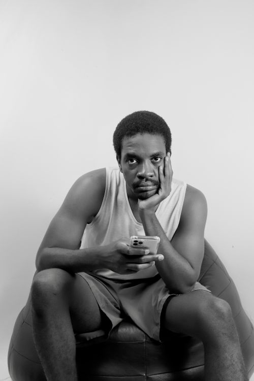 Free Black and white portrait of a man in a tank top sitting thoughtfully with a smartphone. Stock Photo