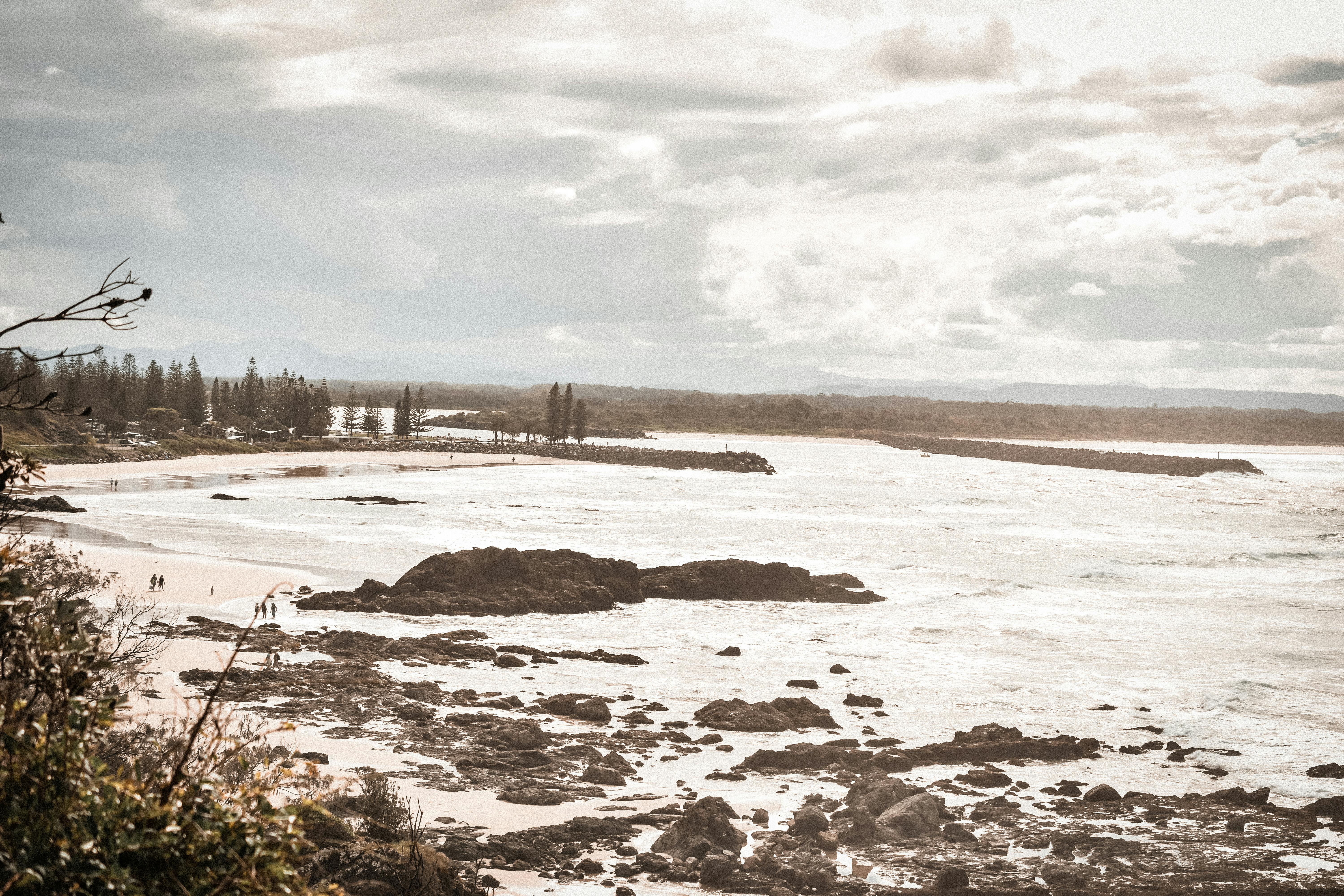 Aerial view of Port Macquarie's rocky coastline with scattered clouds and distant shoreline.