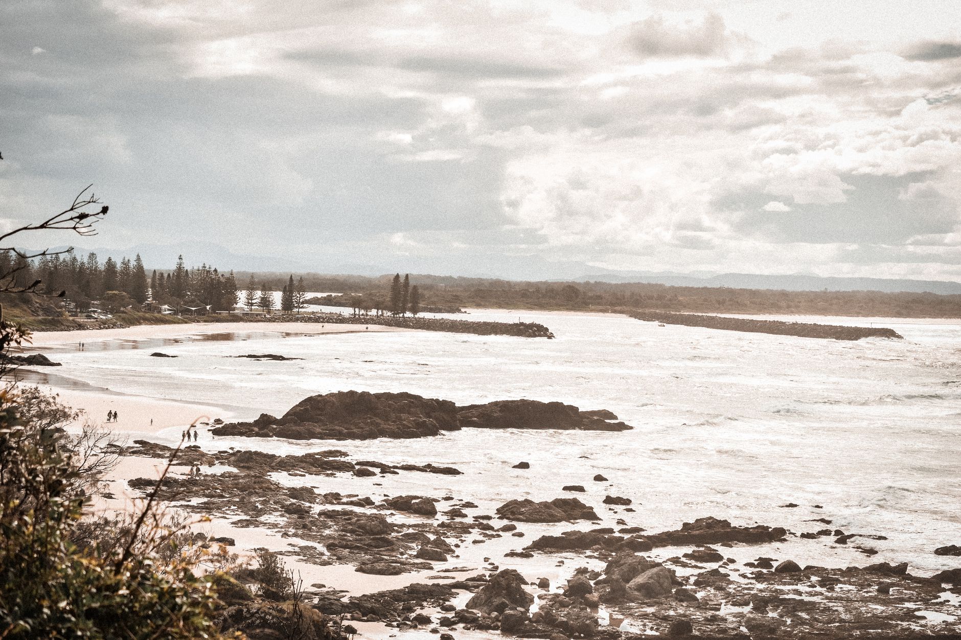 Aerial view of Port Macquarie's rocky coastline with scattered clouds and distant shoreline.