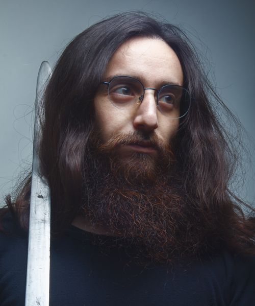 Free Portrait of a bearded man with eyeglasses holding a sword, captured in a studio setting. Stock Photo