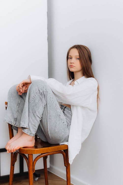 Young Girl in a Simple Trendy Outfit Sitting on a Wooden Chair 