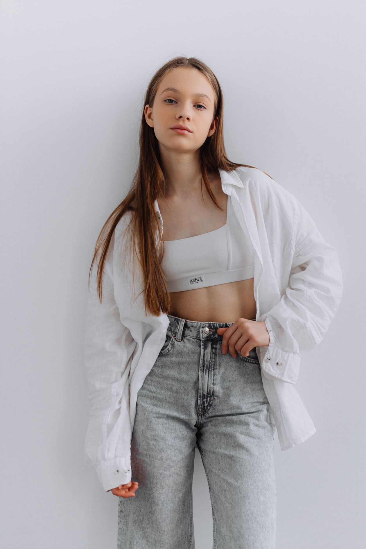 Young woman in minimalist white shirt and jeans studio setting clean aesthetic outfit