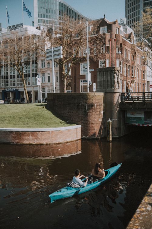 Free Two people kayak along a serene canal amid urban architecture and greenery. Stock Photo