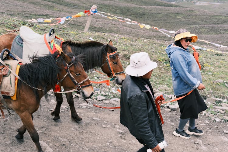 People In Hats Leading Horses On Dirt Road