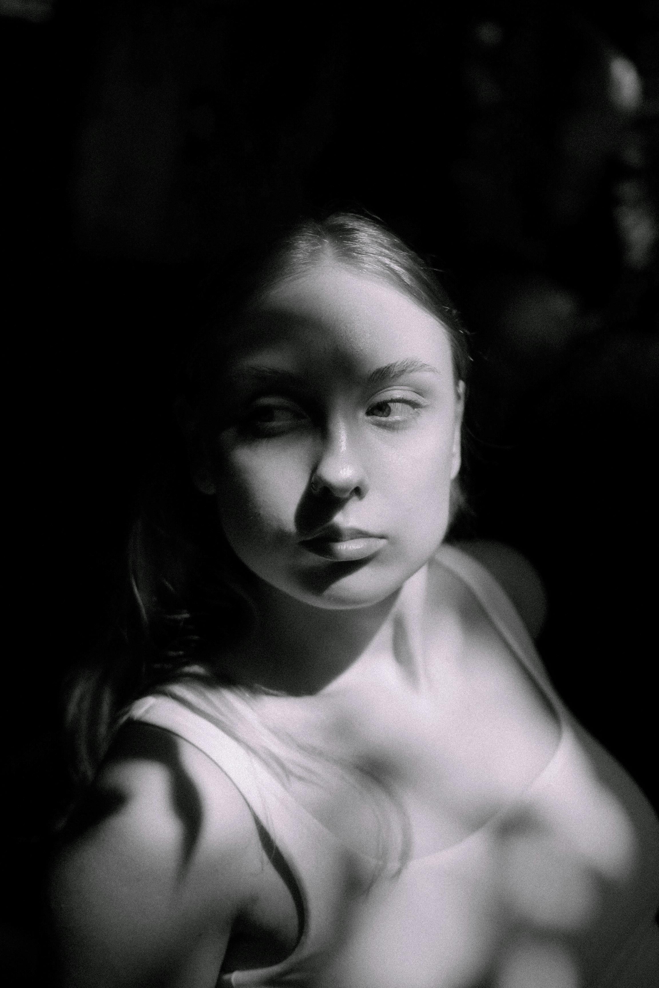 Artistic black and white portrait of a woman in sunlight creating dramatic shadows.