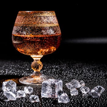 A luxurious shot of whiskey in a crystal glass surrounded by ice cubes on a textured surface.