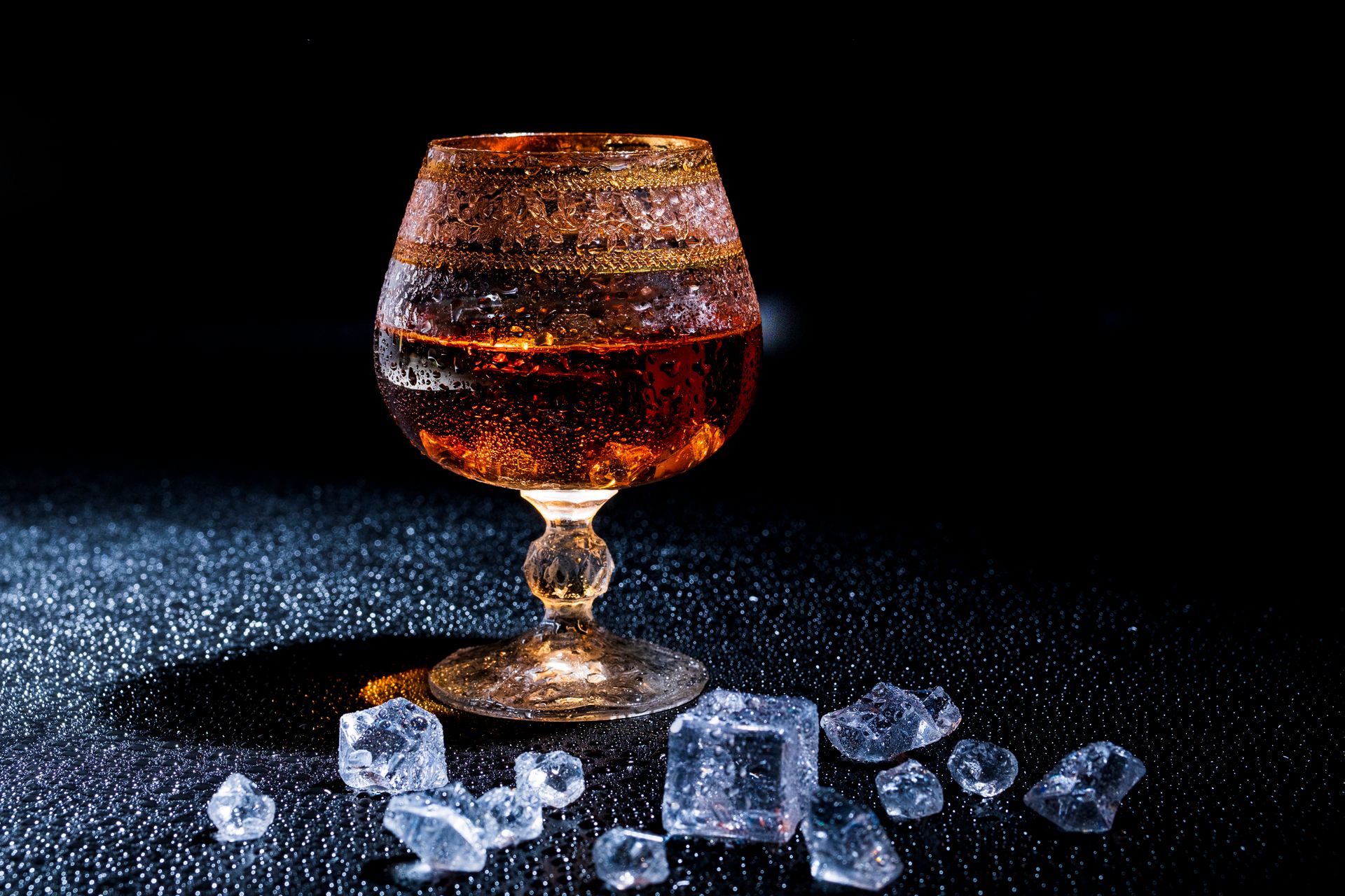 A luxury whiskey glass with ice cubes, elegantly displayed on a textured black surface, perfect for bar and drink themes.