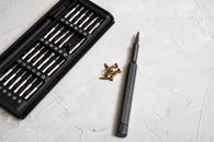 Close-up of a precision screwdriver kit with various bits and screws on a light textured background.