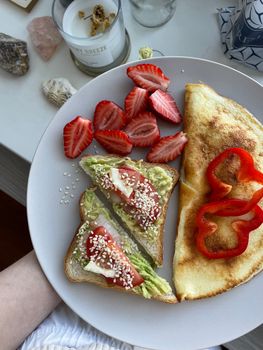 A delicious breakfast plate featuring avocado toast, strawberries, and an omelette.