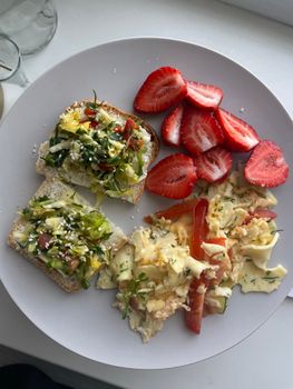 A wholesome breakfast plate featuring avocado toast, scrambled eggs, and fresh strawberries.