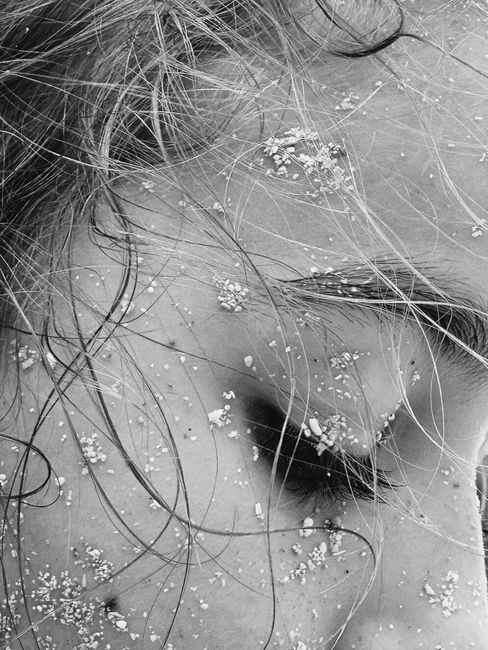Artistic black and white close-up of a woman's face with sand-dusted skin and hair.