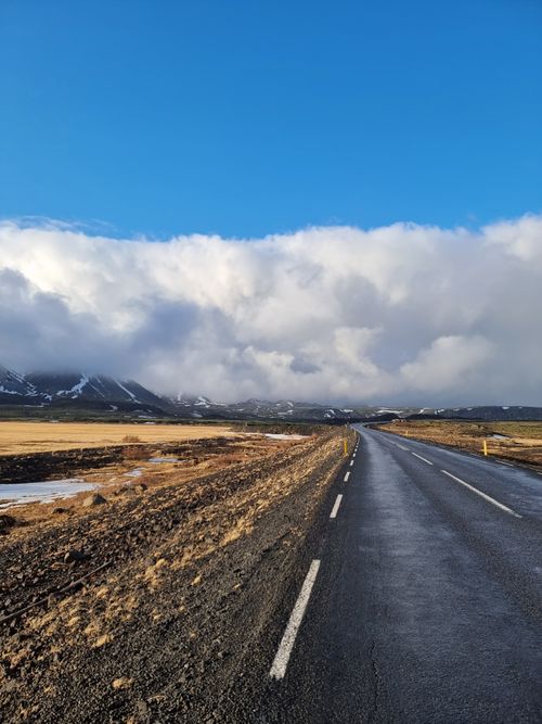 Free A stunning view of an asphalt road stretching through a cloudy valley with distant mountains. Stock Photo