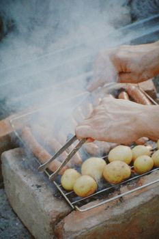 Close-up of hands grilling sausages and potatoes outdoors in Talgar, Kazakhstan.