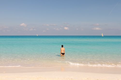 Free A woman stands on a tropical beach with turquoise water, enjoying a serene vacation moment. Stock Photo