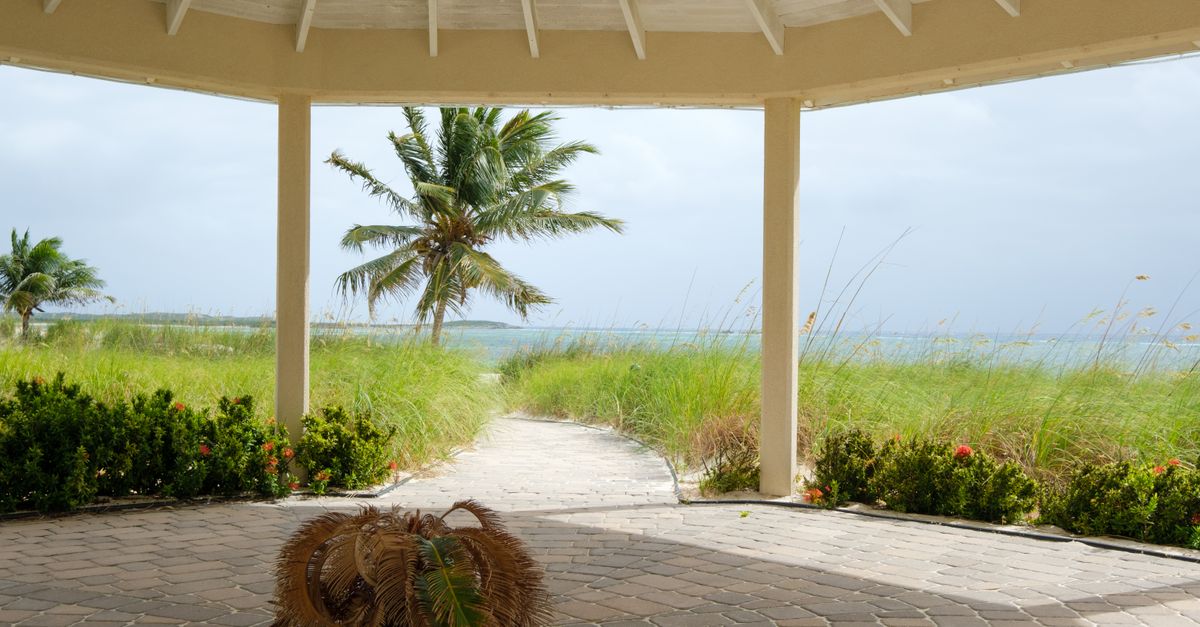 Serene view from a gazebo overlooking a tropical beach with palm trees and blue waters.
