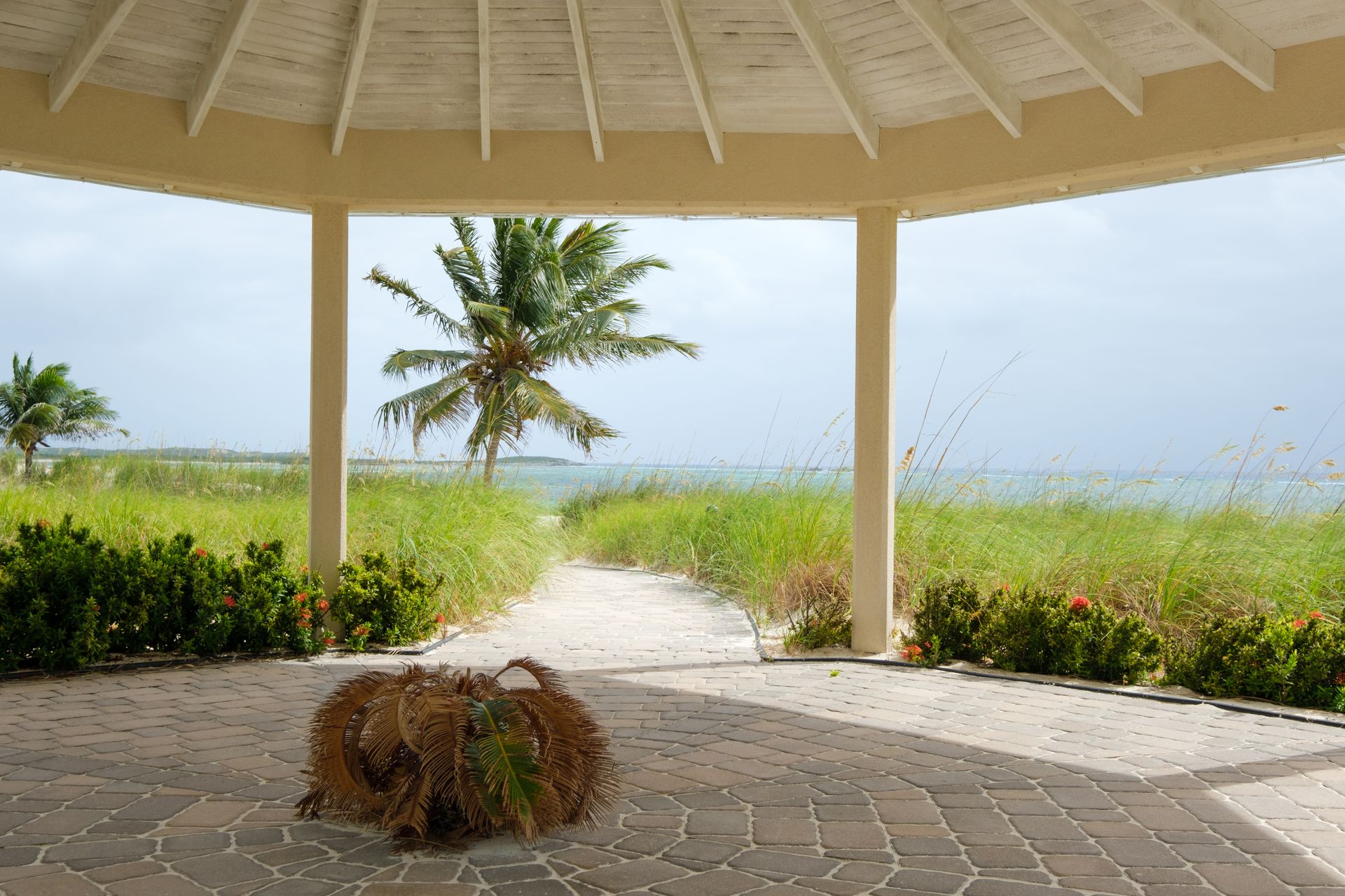 Serene view from a gazebo overlooking a tropical beach with palm trees and blue waters.