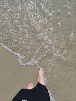 Overhead view of feet by the sea on a sunny beach day.