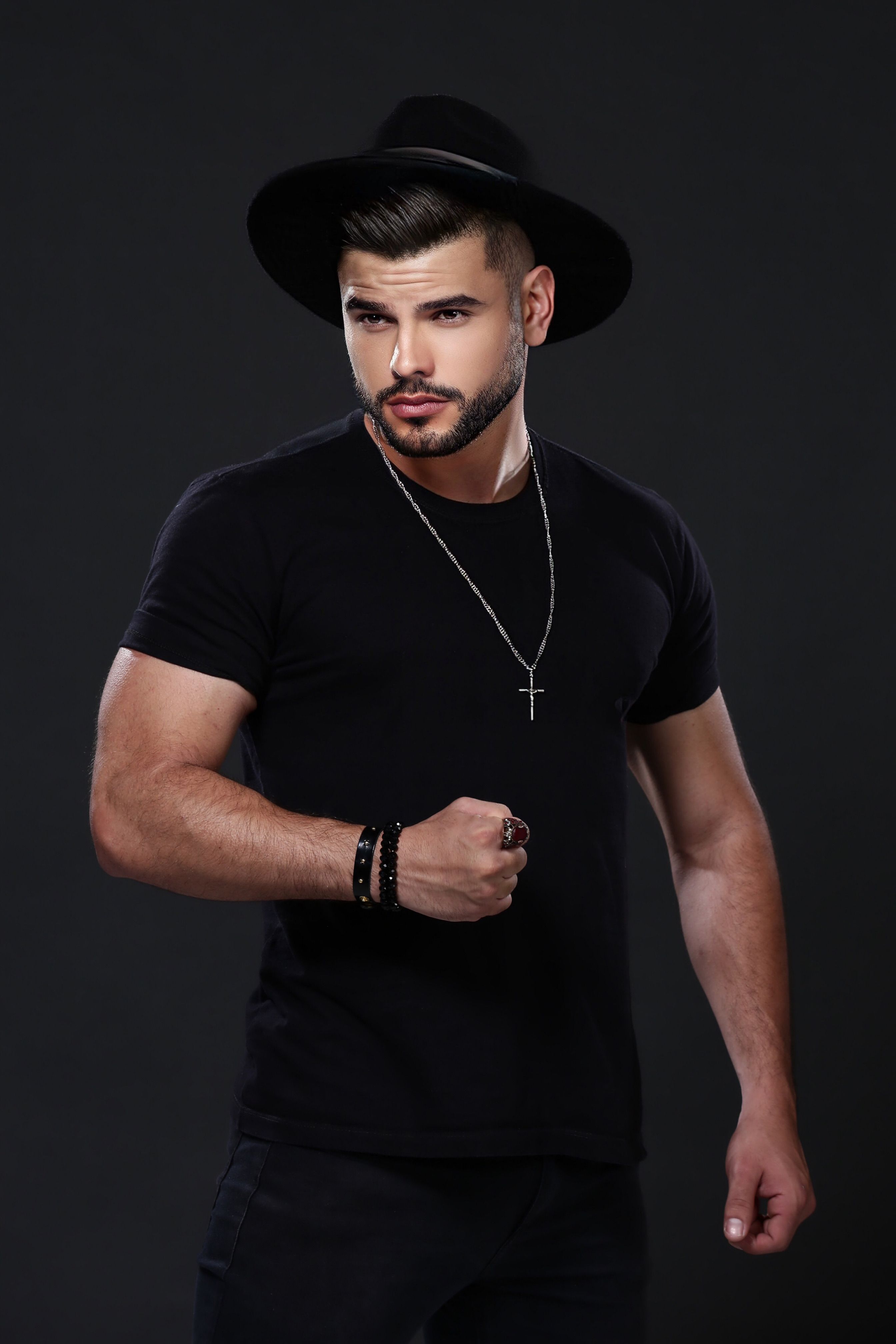 Fashionable man wearing a black hat and t-shirt with necklace on black background.