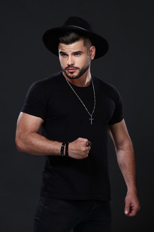 Free Fashionable man wearing a black hat and t-shirt with necklace on black background. Stock Photo