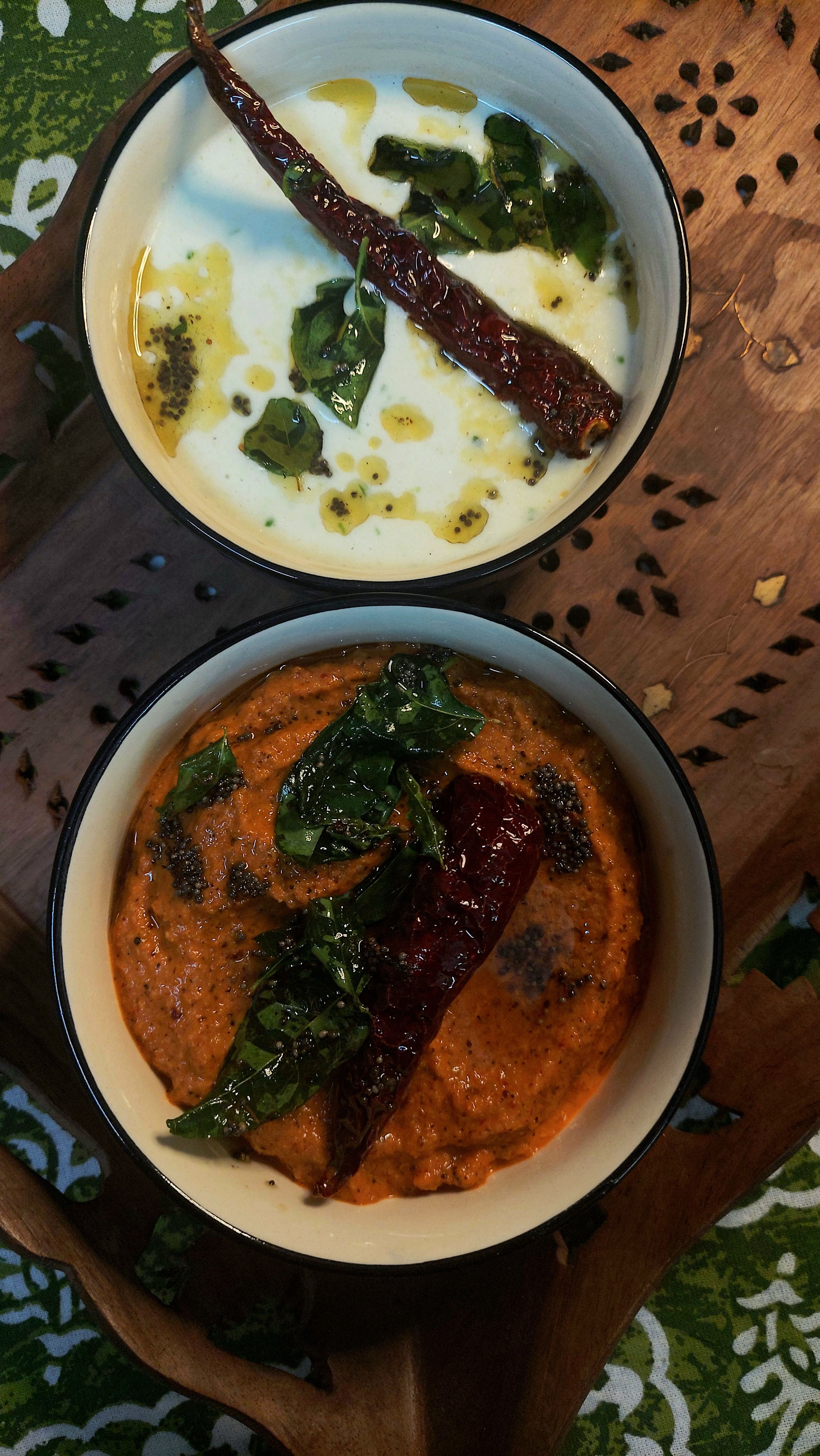 Top view of savory Indian yogurt and tomato chutneys garnished with spices.
