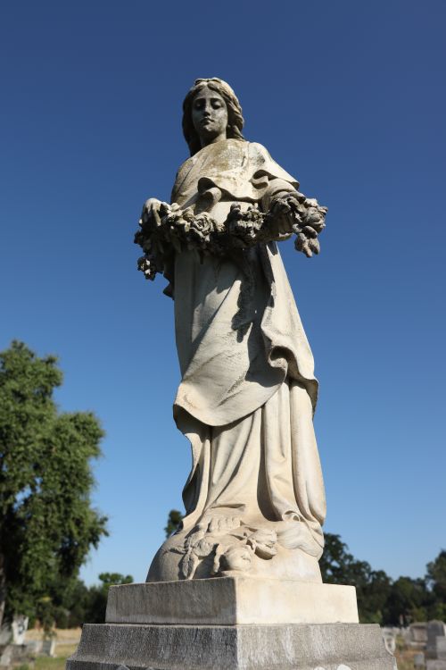 Free A beautifully carved stone statue of a woman holding flowers, emphasizing tranquility in a cemetery. Stock Photo
