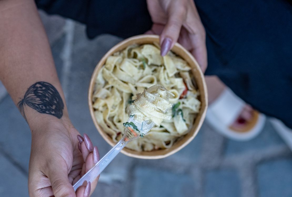 Free Close-up of a woman holding a bowl of pasta with tattooed hands, enjoying a meal outdoors. Stock Photo