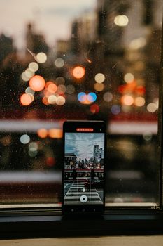 Smartphone photographing vibrant Toronto cityscape through a rainy window at night.