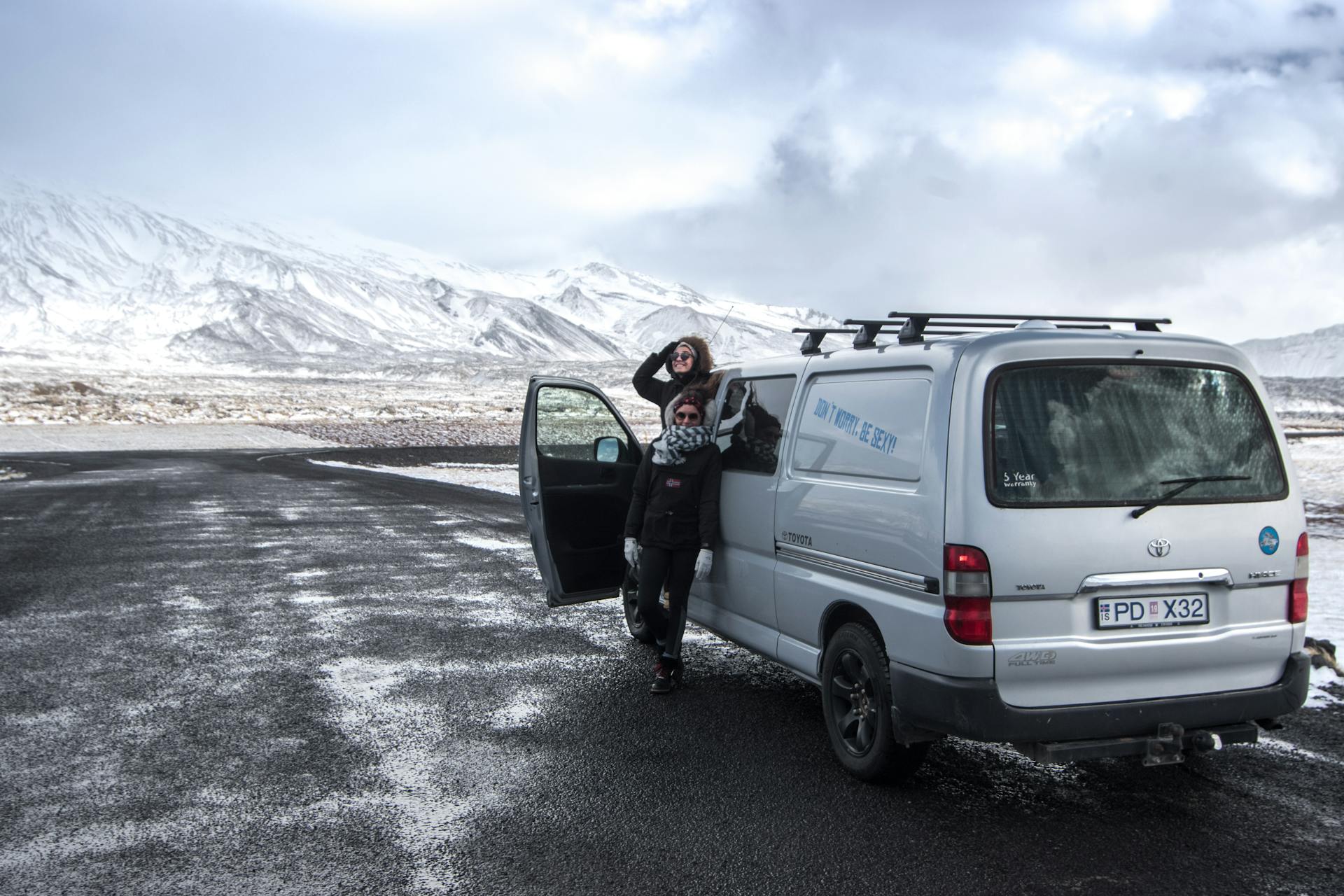 Two travelers enjoying a winter road trip in Iceland's snowy landscape with a camper van.