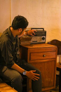 Man tuning a vintage radio in a cozy, retro-themed room.