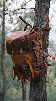 A rustic leather backpack hangs on a tree in a forest setting, ideal for outdoor adventure themes.