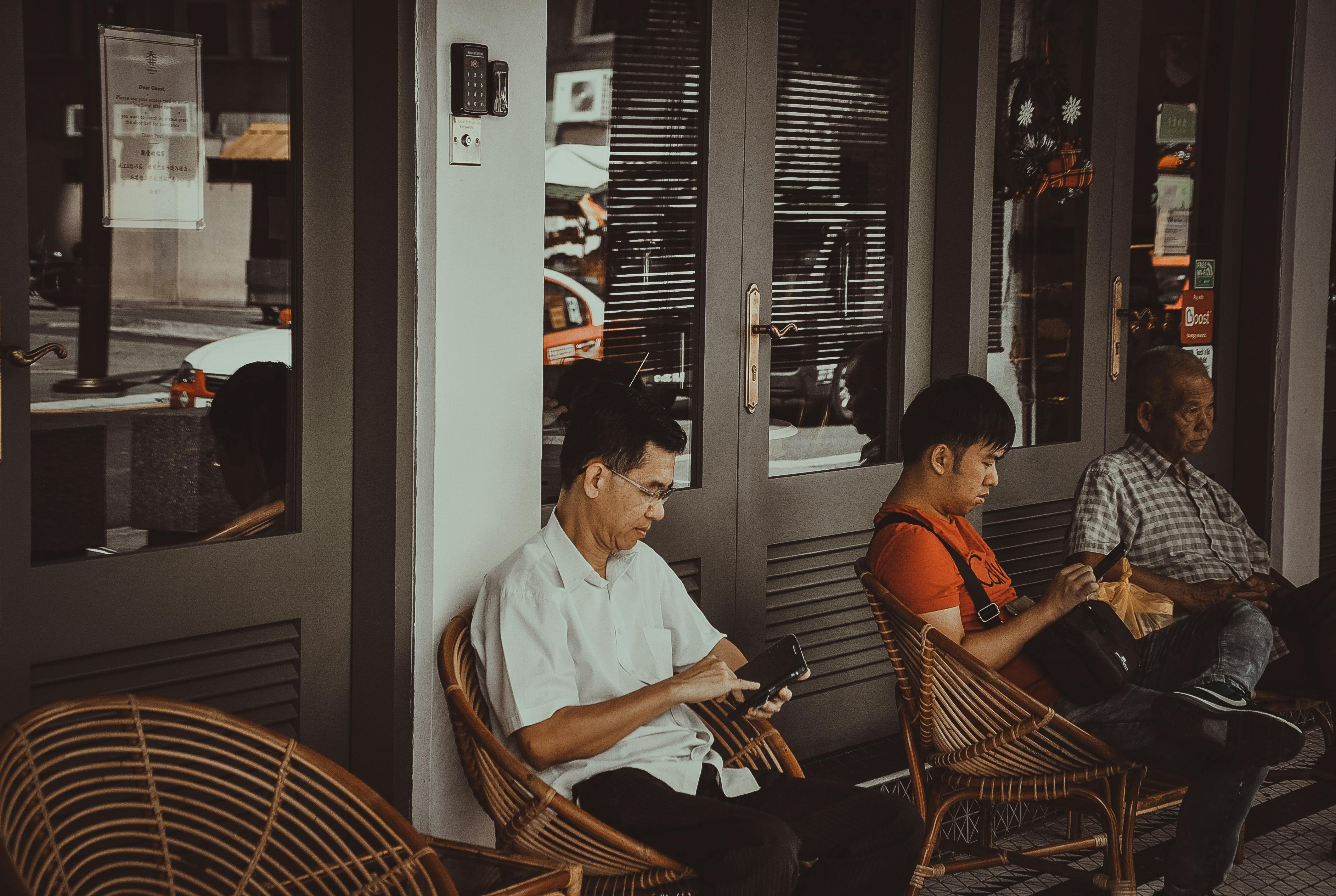 咖啡馆外，三名男子坐在椅子上玩手机