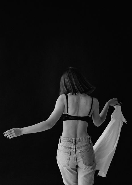 Artistic black and white portrait of a woman posing in fashion attire with a dark background.