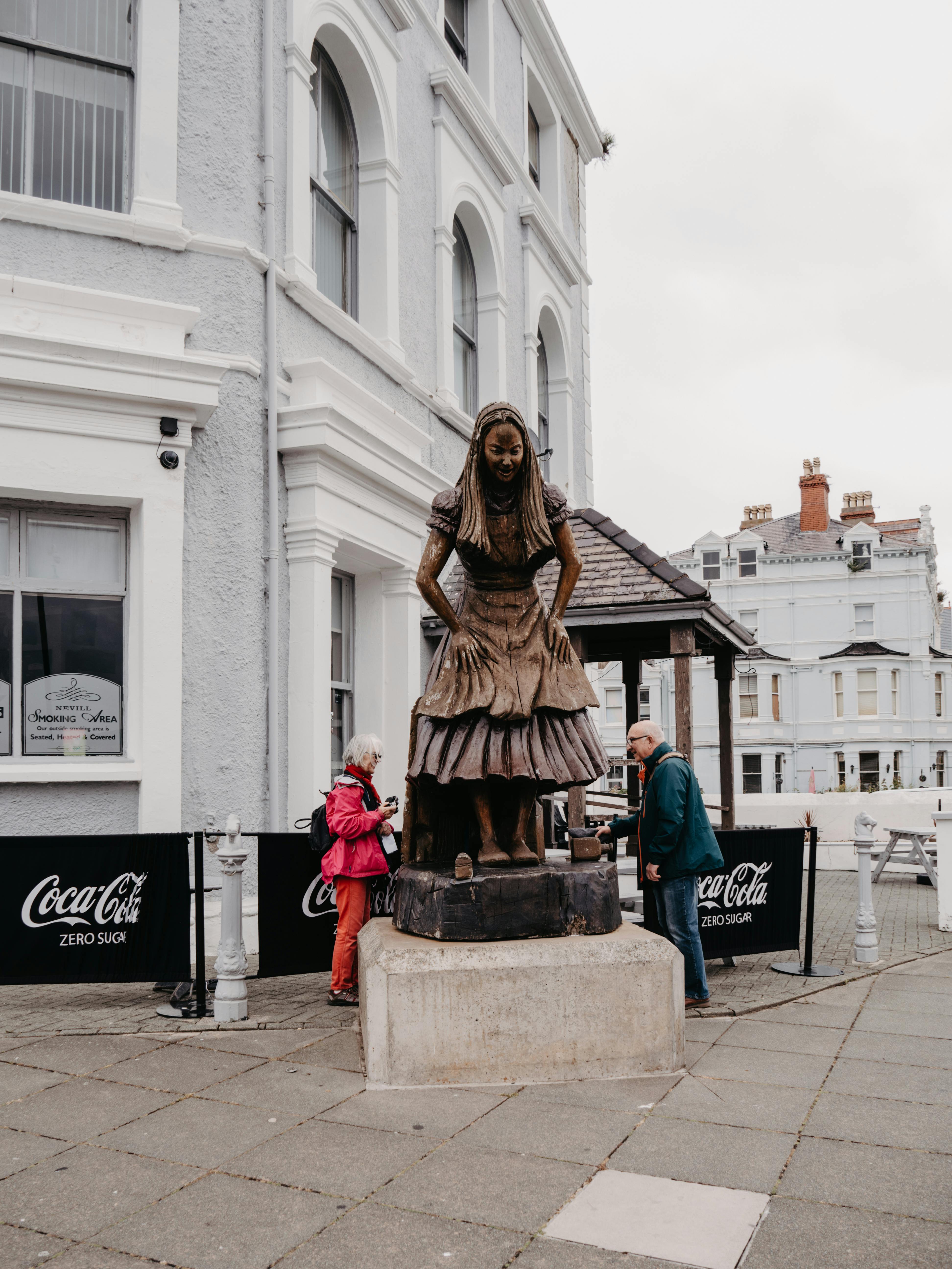 Bronze statue of Alice in Wonderland on a city street in Llandudno, Wales.