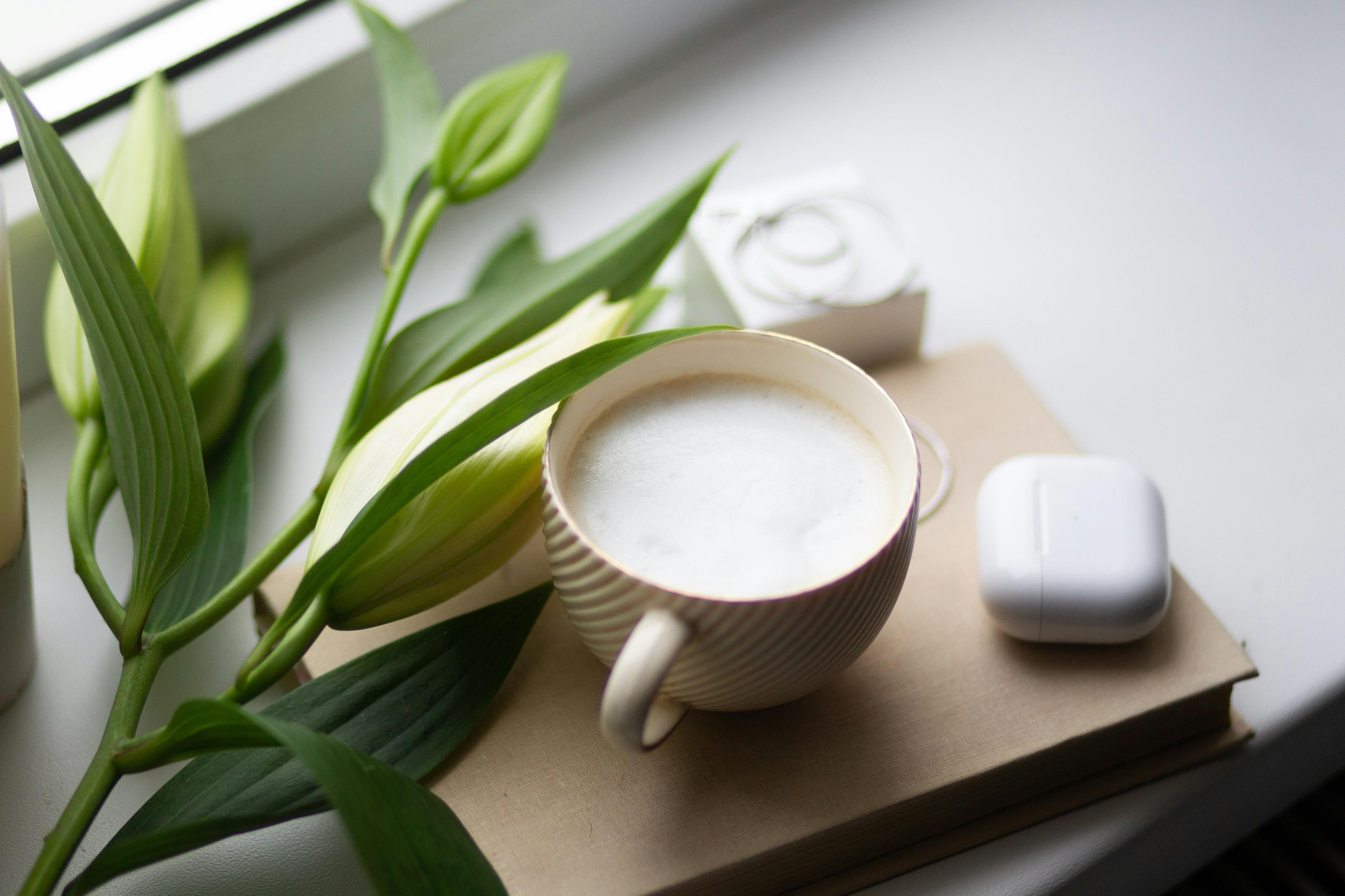 how to make sweet foam for coffee - Serene scene with a coffee mug, book, and lilies on a windowsill, ideal for relaxation themes.