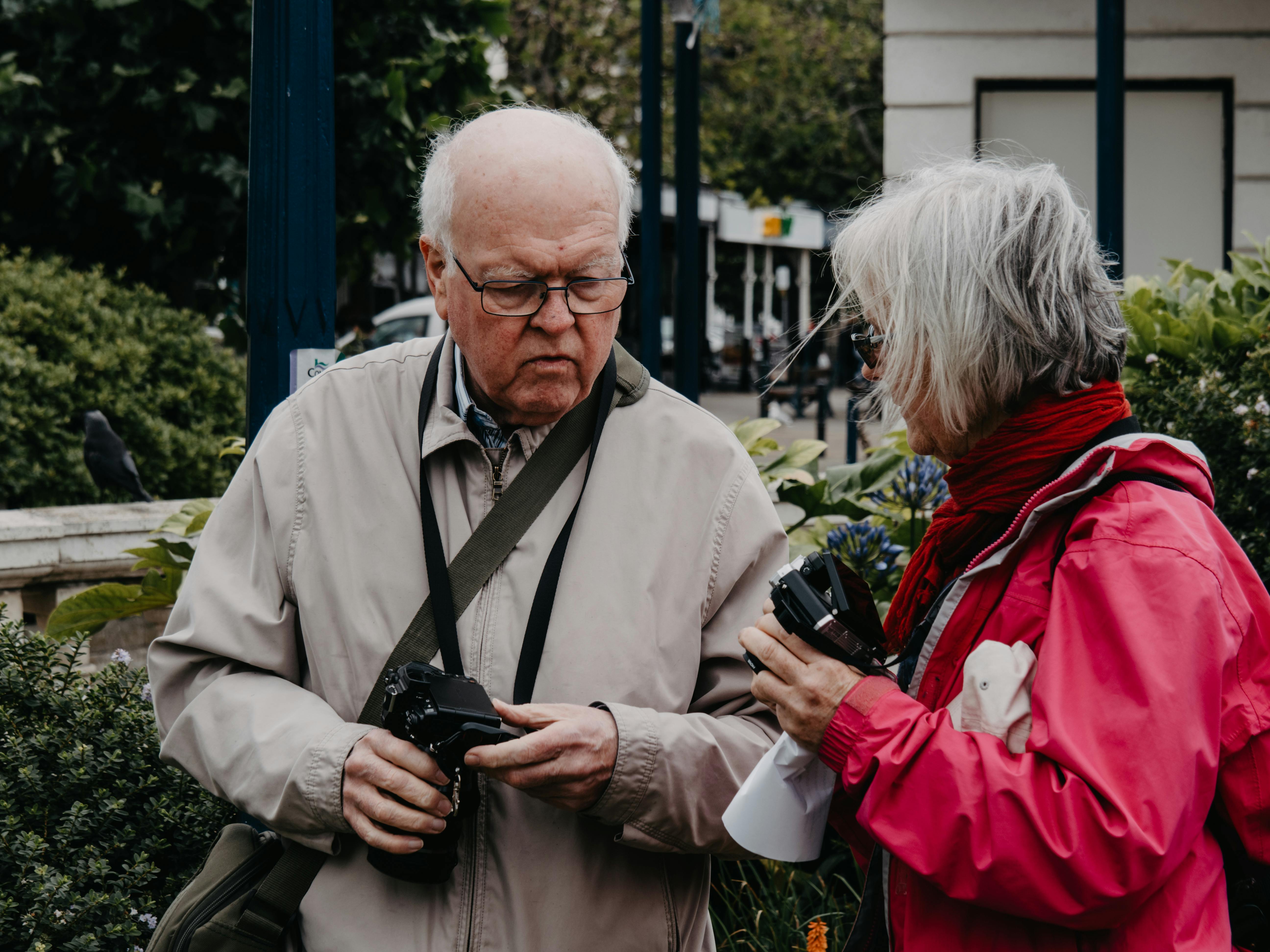 An elderly couple discussing photography outdoors, surrounded by greenery.