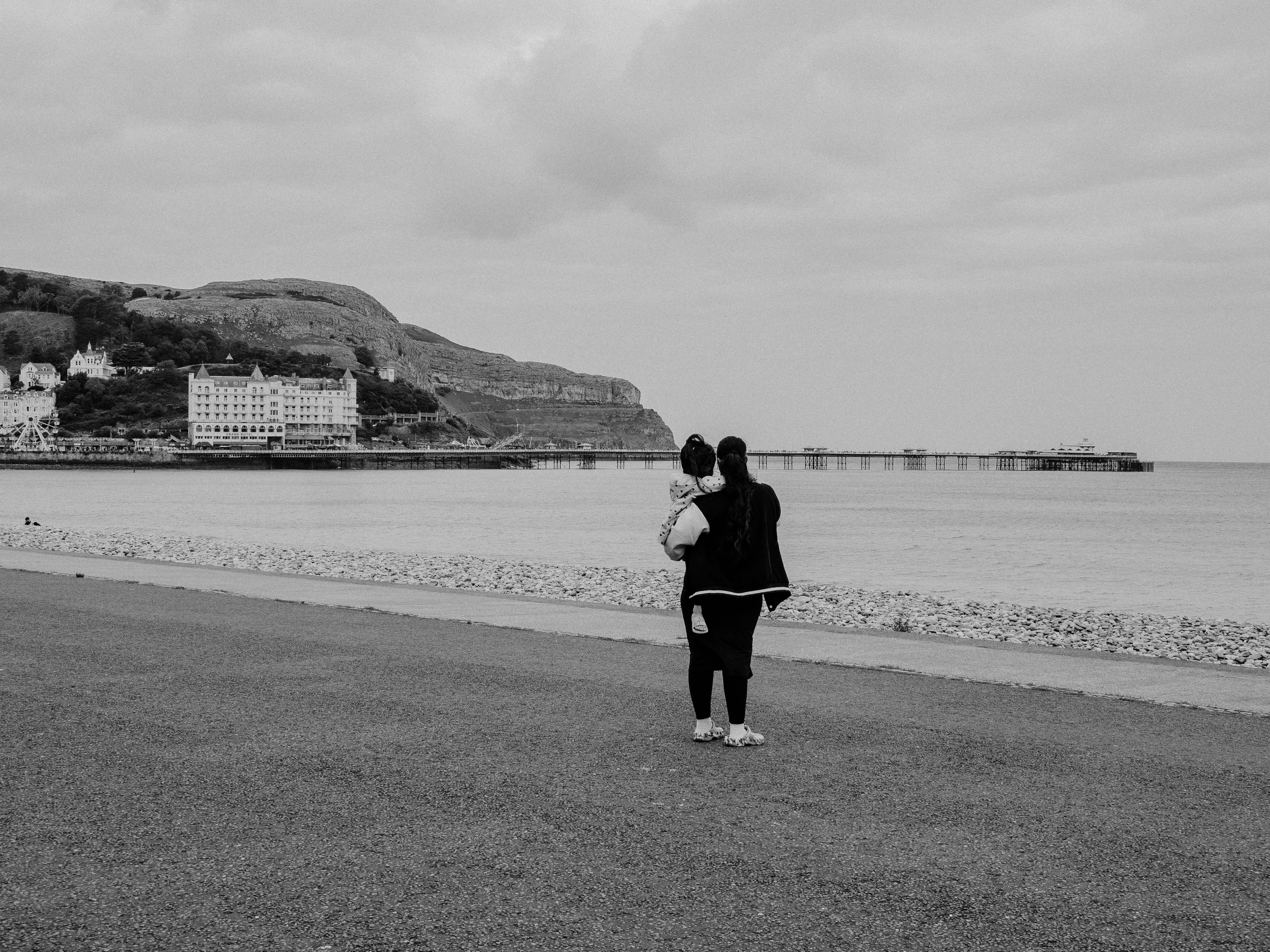 A mother holding her child looks out over the sea at Llandudno, Wales.