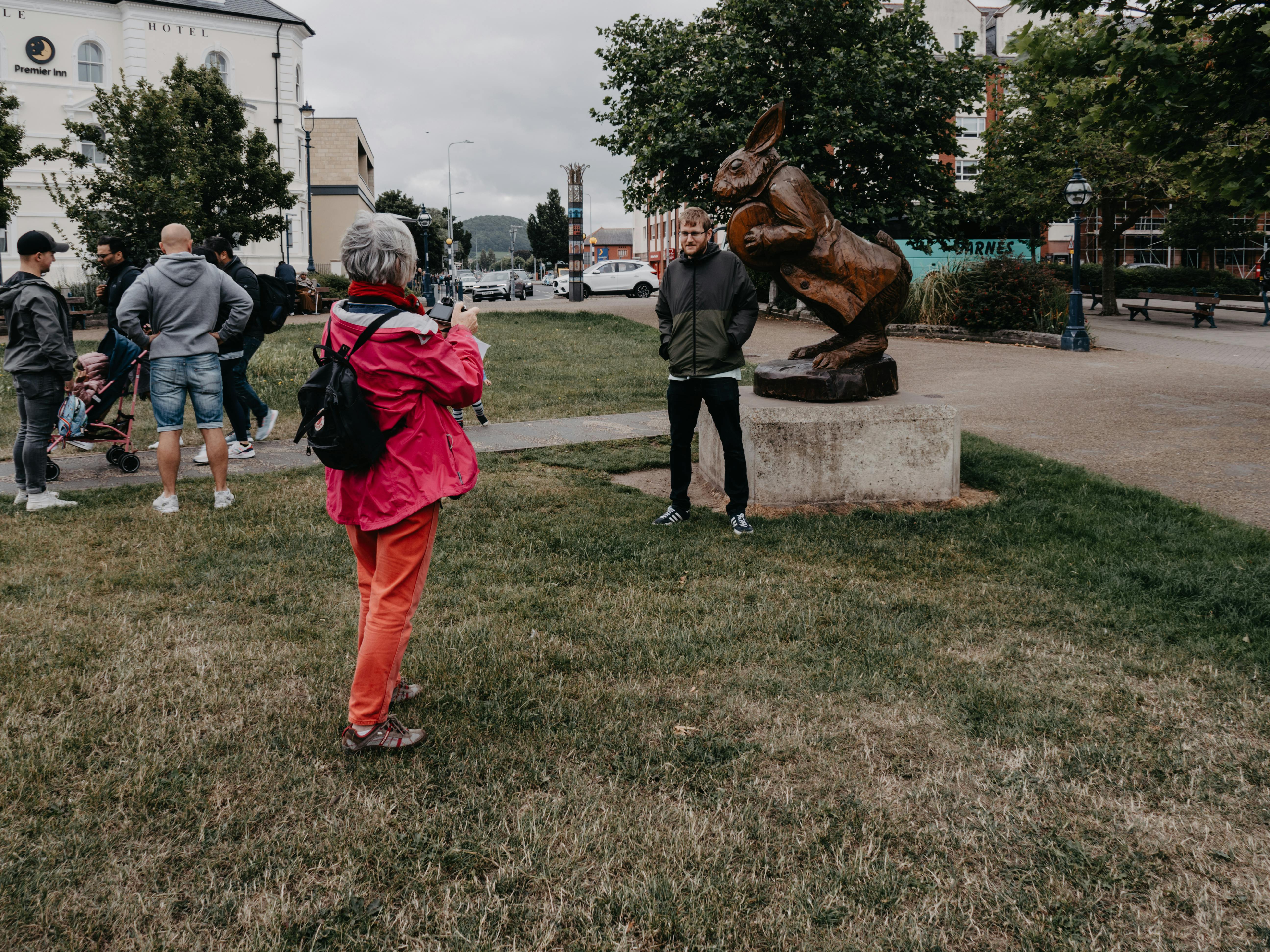 People pose with a white rabbit sculpture in a park in Llandudno, Wales, capturing a whimsical moment.