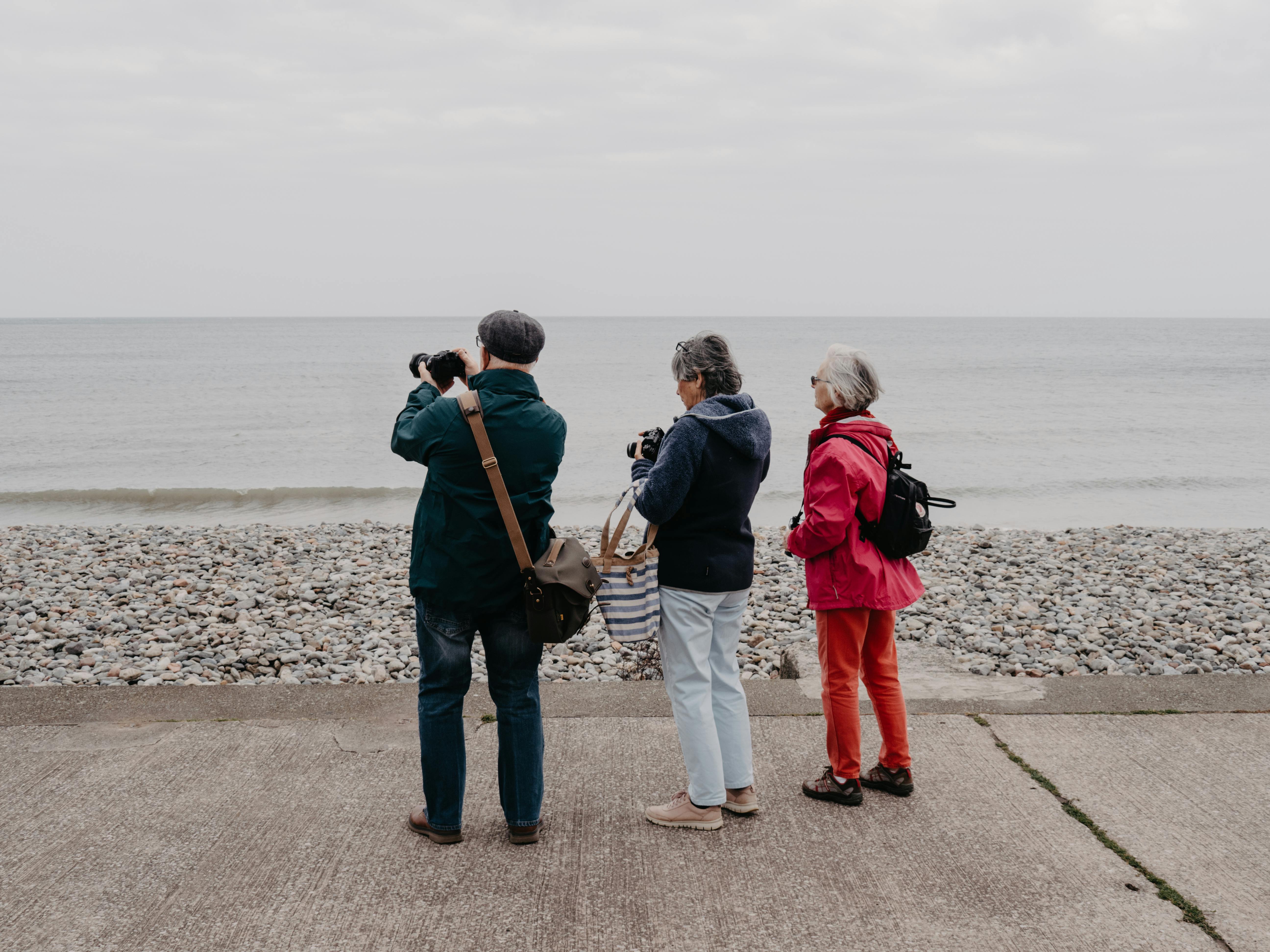 Three senior tourists with cameras capturing the scenic coast of Llandudno, Wales.