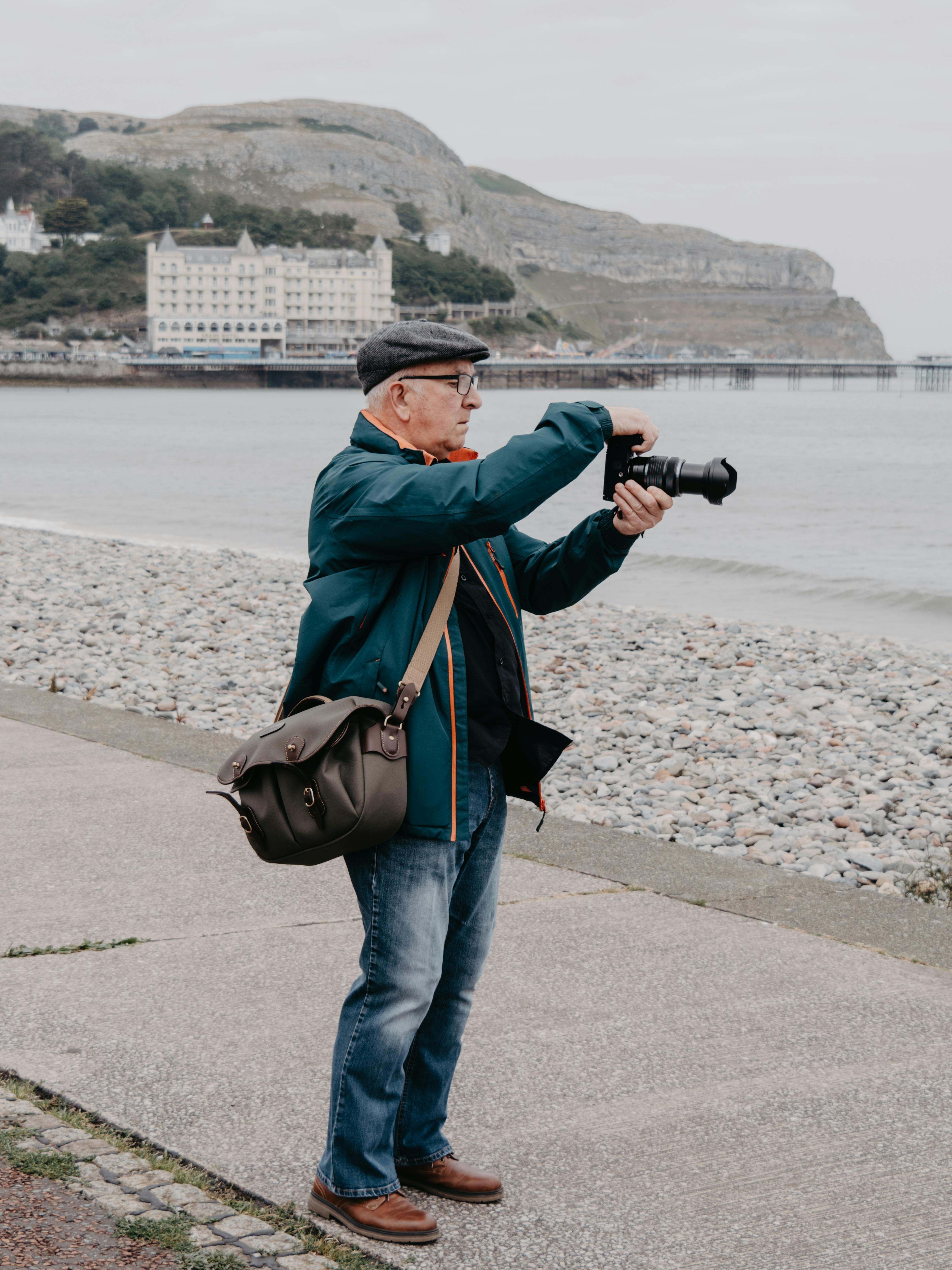 Senior man captures Llandudno's scenic coast with his camera by the sea.